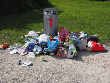 Picture of a full trashcan by the side of the road. The trashcan is so full that it is overflowing.