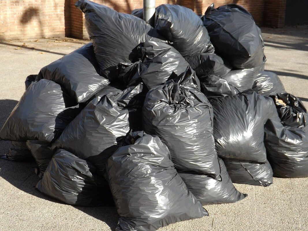 Picture of a dozen garbage bags lying on the side of the road. 